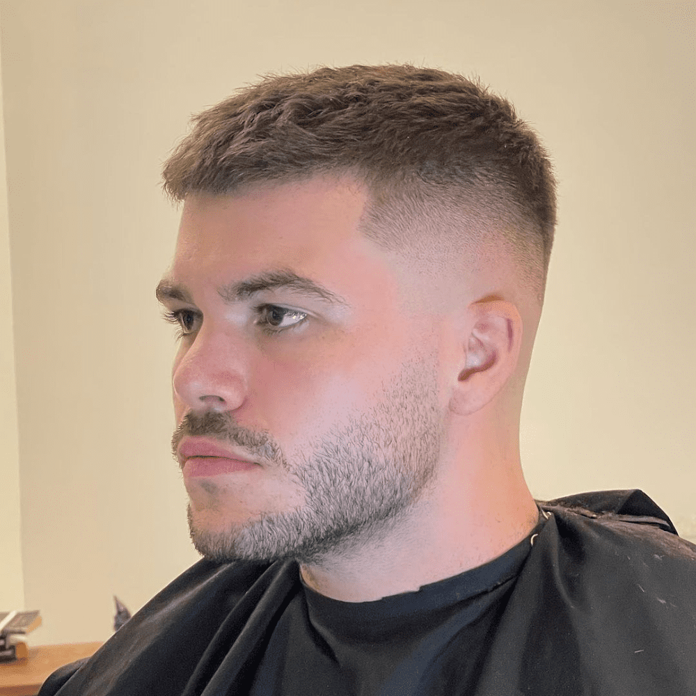 Man with a short fade haircut featuring a crew cut and skin fade. The hairstyle showcases a clean, sharp skin fade on the sides and back, blending into the short, textured crew cut on top. This classic and stylish look is ideal for men's hairstyles in 2024, offering a polished and modern appearance.