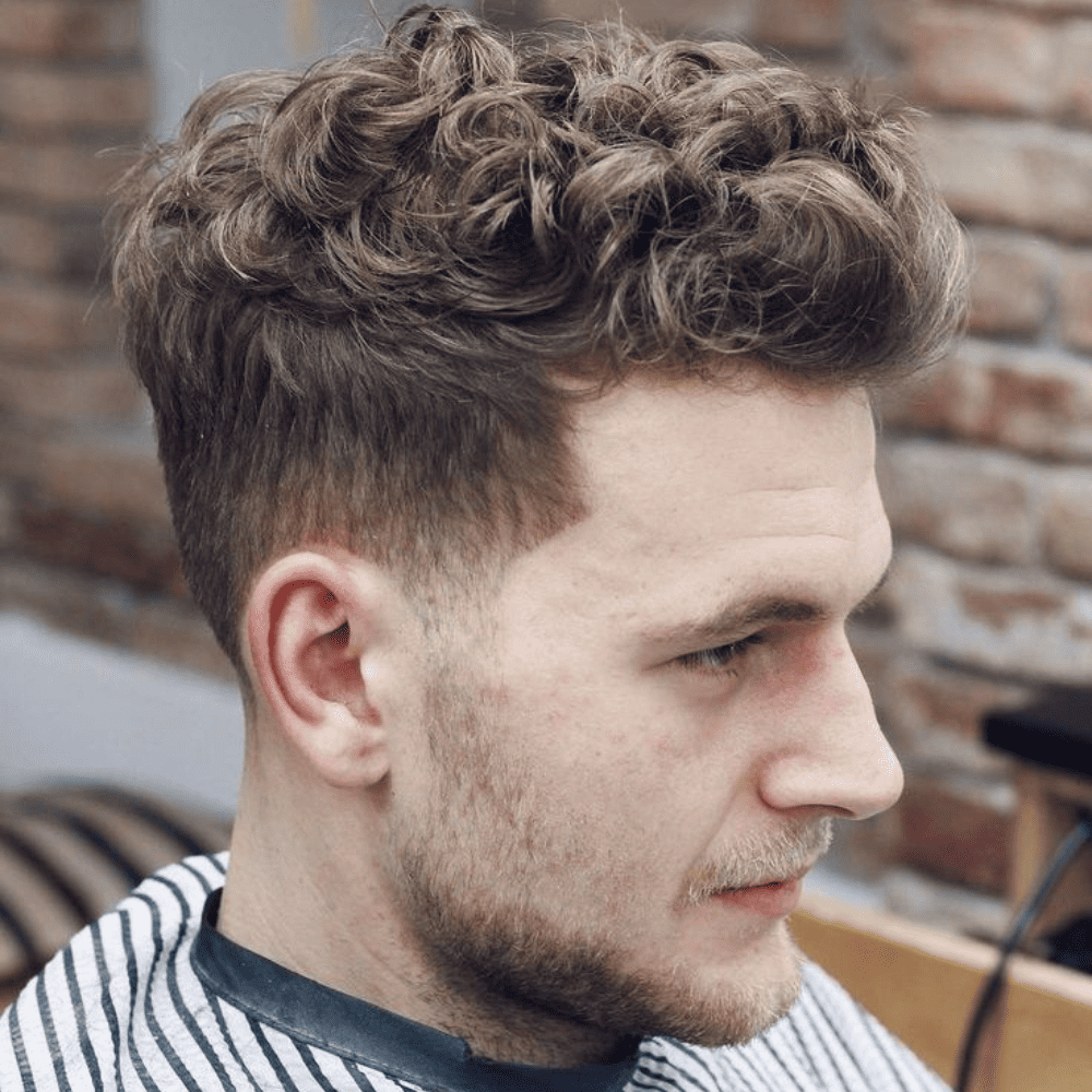 This image showcases a stylish curly quiff haircut for men, featuring voluminous curls on top with a neat fade on the sides. The hairstyle perfectly complements a medium-length beard, offering a balanced and fashionable look. Ideal for men with naturally curly hair, this trendy haircut provides a modern and sophisticated appearance suitable for various face shapes. This look combines classic elegance with contemporary flair, making it a popular choice among men seeking a versatile and polished style in 2024.