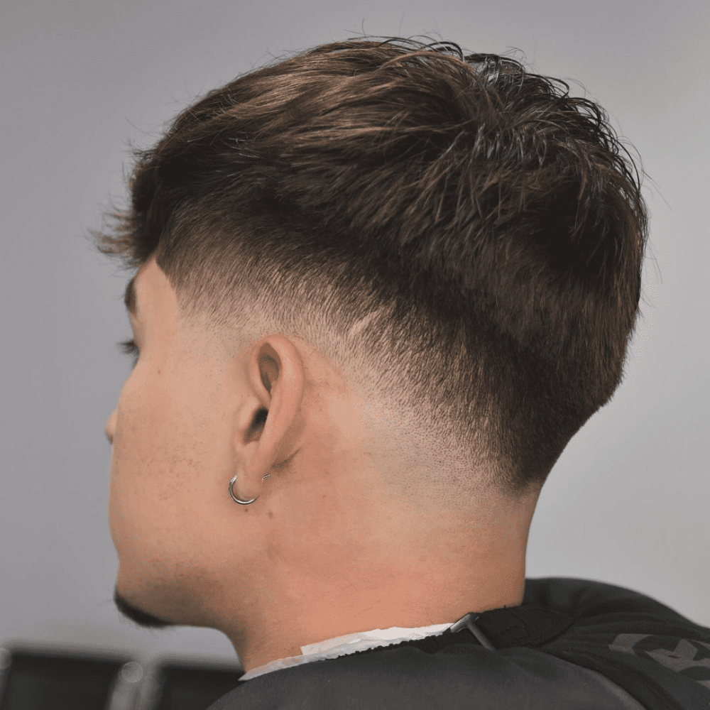 Close-up side view of a stylish drop fade haircut on a young man with dark brown hair. The fade tapers gradually behind the ear, highlighting the clean lines and modern look. Perfect example of a trendy drop fade in the drop fade vs low fade comparison. drop fade haircut.