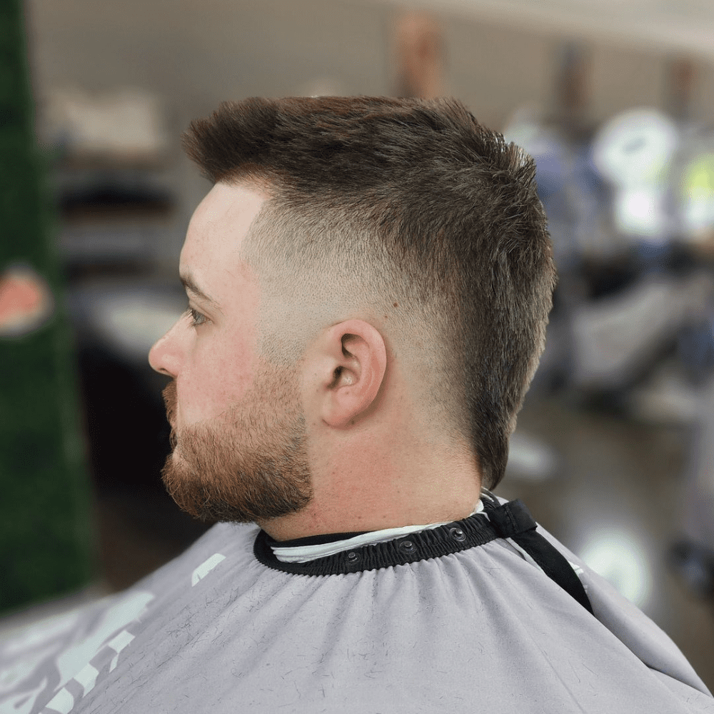 Side profile of a man with a Faux Hawk Fade haircut, featuring a strip of longer hair running from the front to the back of the head, with the sides and back faded for a clean contrast. The hairstyle highlights a modern and edgy look, perfect for men seeking trendy fade haircuts