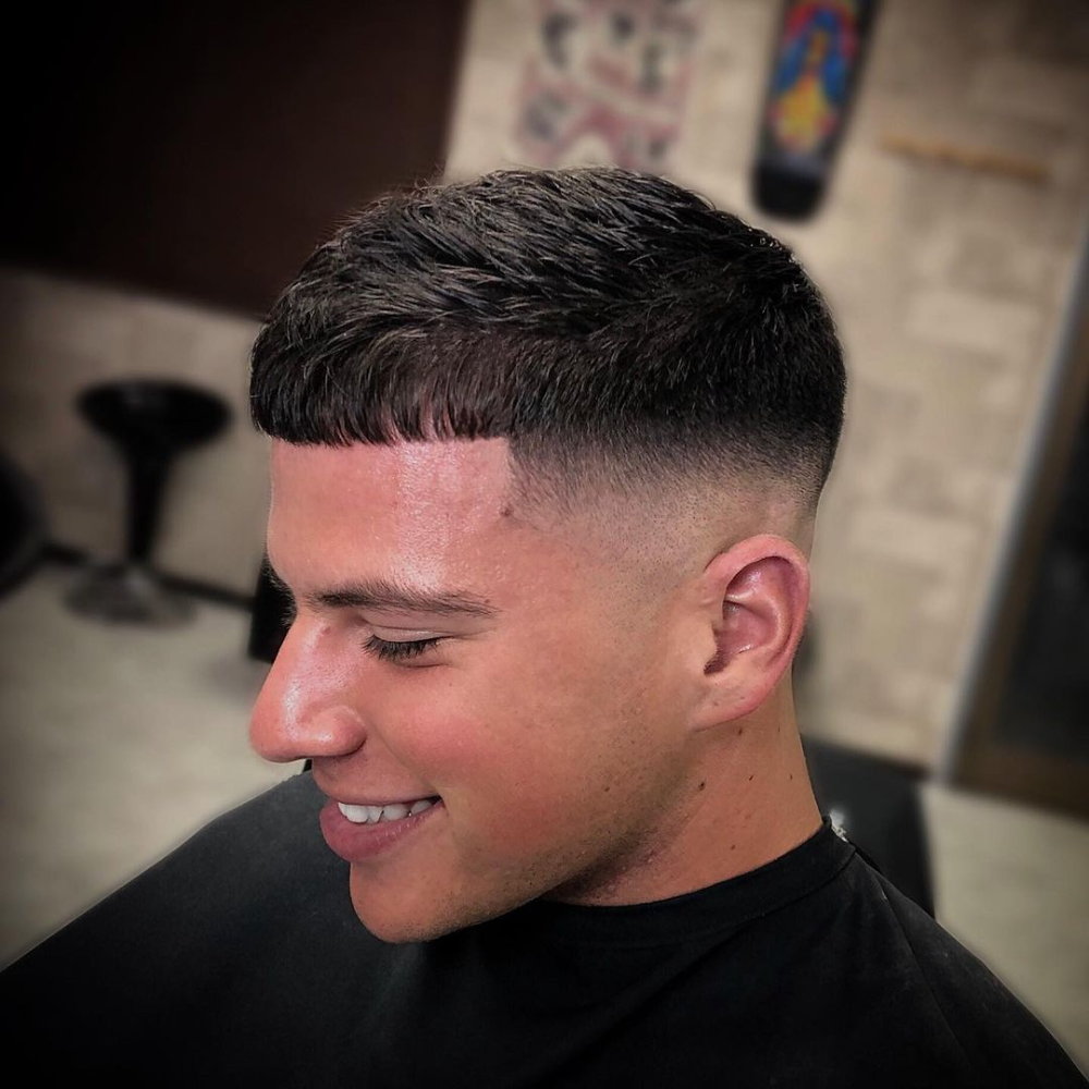 Man with a short fade haircut featuring a French crop. The hairstyle includes a clean fade on the sides and back, blending into the short, straight fringe on top. This modern and stylish look is perfect for men's hairstyles in 2024, offering a sharp and polished appearance.