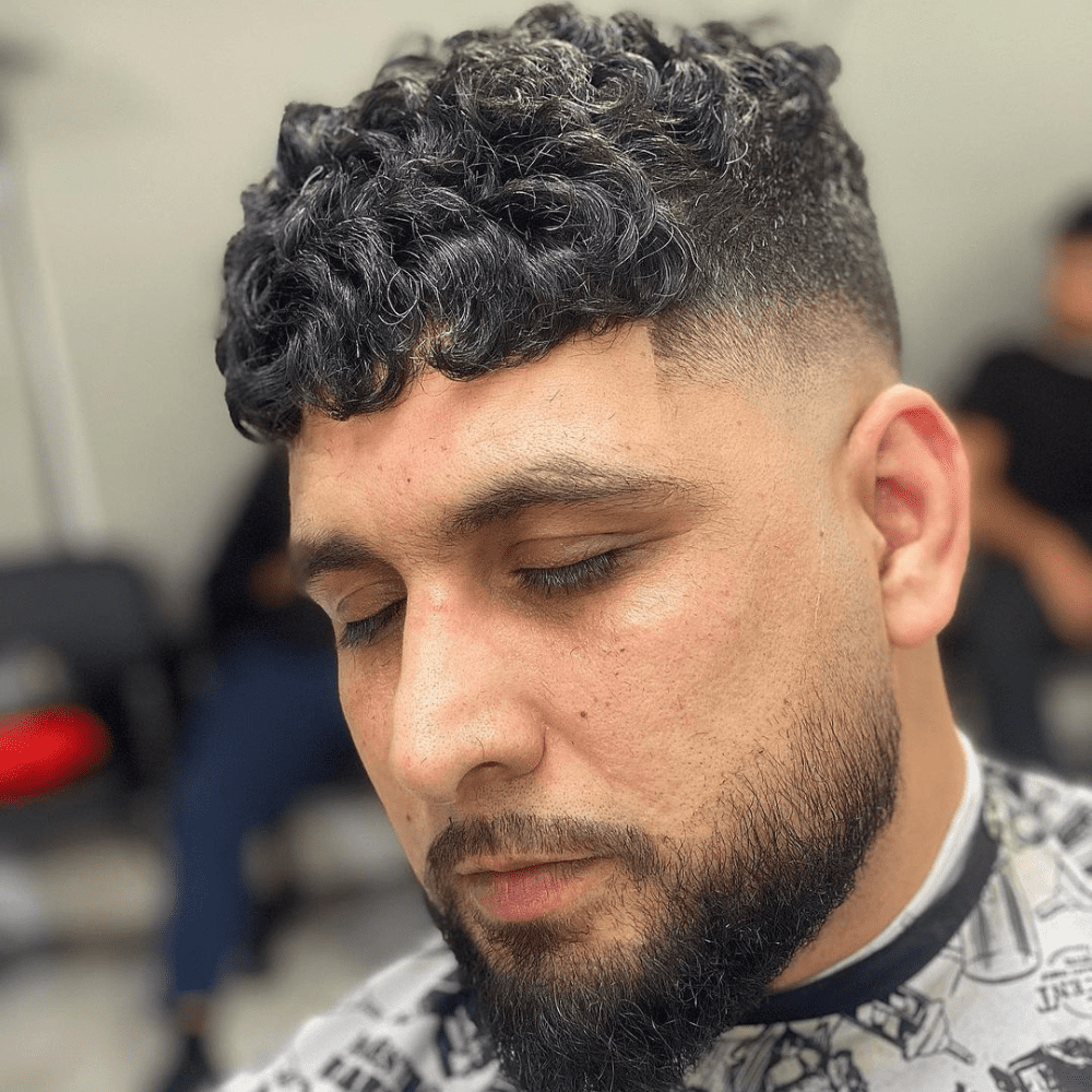 Man with a short fade haircut featuring a high drop fade and curly top. The hairstyle showcases a clean high drop fade on the sides and back, seamlessly blending into the voluminous, curly hair on top. This stylish and modern look is perfect for men's hairstyles in 2024, highlighting the texture and volume of curly hair.