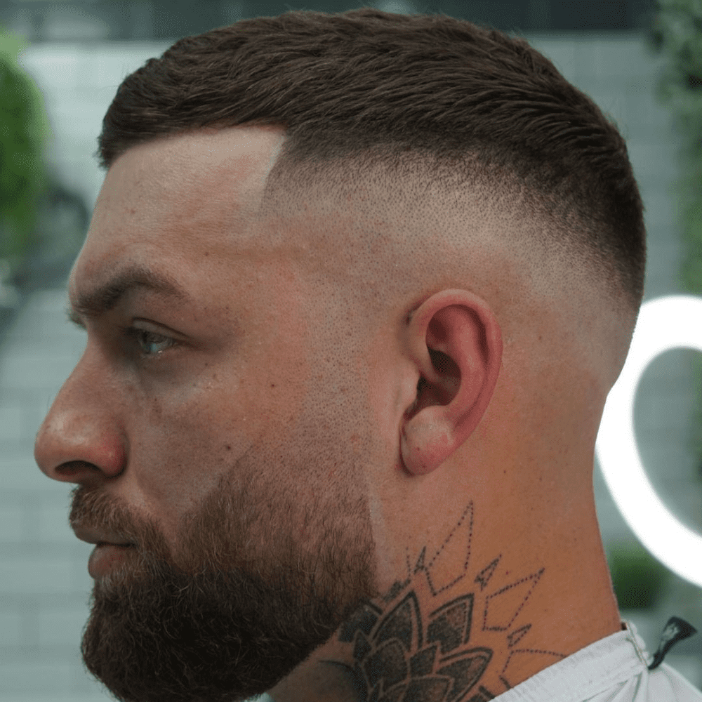 Side profile of a man with a High Drop Fade haircut, featuring short, textured hair on top and a high fade that drops down behind the ears. The hairstyle offers a bold and modern look, making it an ideal choice for men seeking stylish fade haircuts.