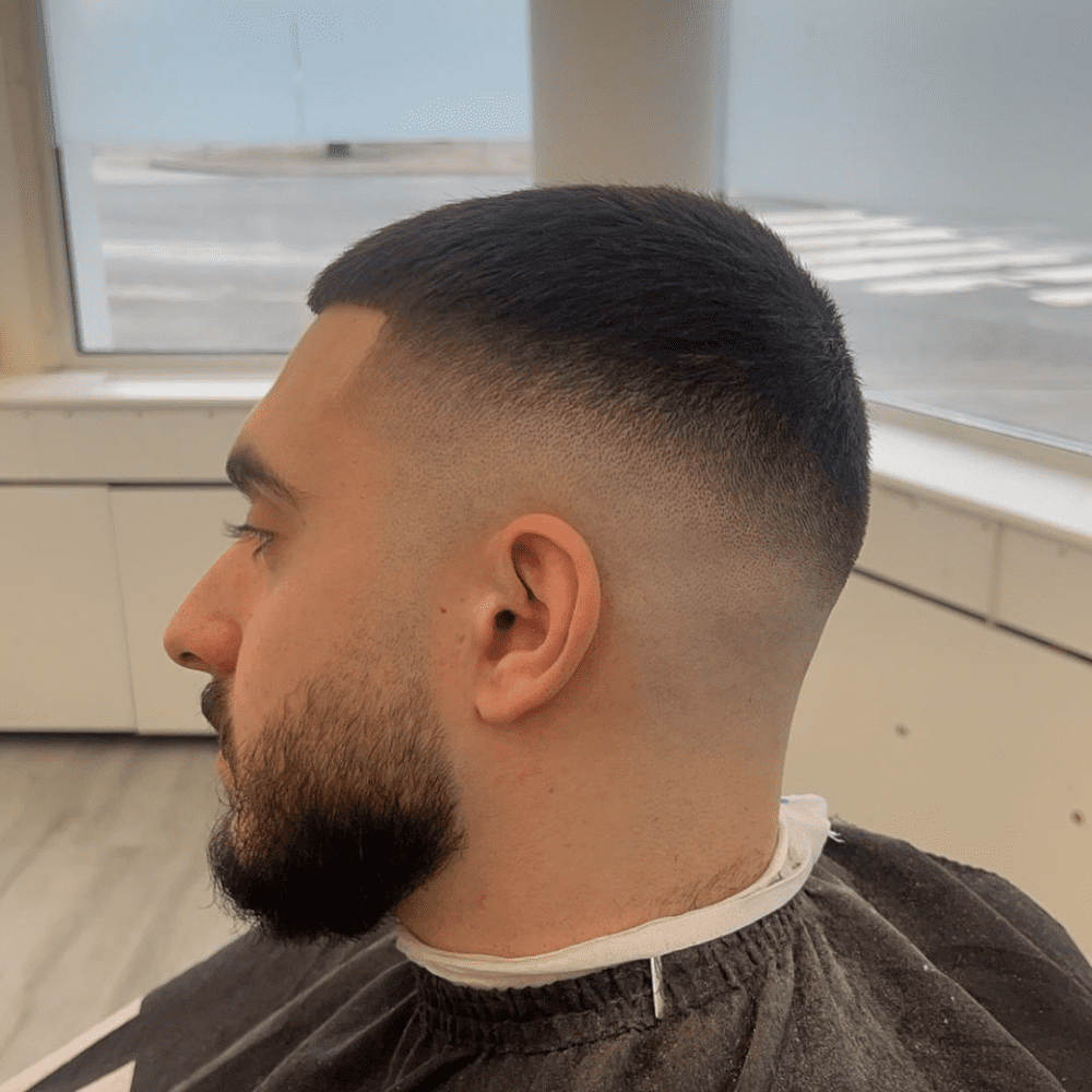 Side profile of a man with a high skin fade haircut, showcasing the smooth gradient from the closely shaved sides to the slightly longer hair on top, paired with a well-groomed beard.