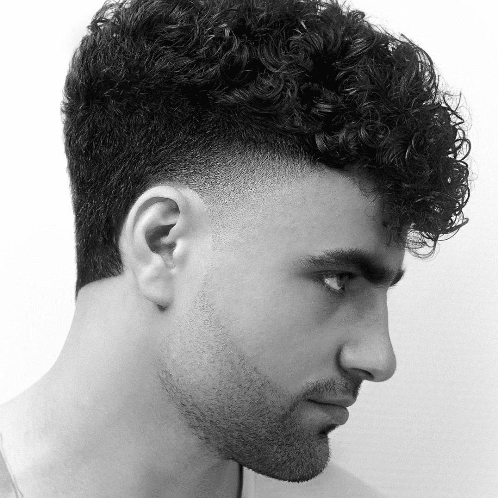 Side profile of a man with a high taper fade haircut and curly hair on top, showcasing the clean and sharp transition from the longer textured curls to the closely shaved sides