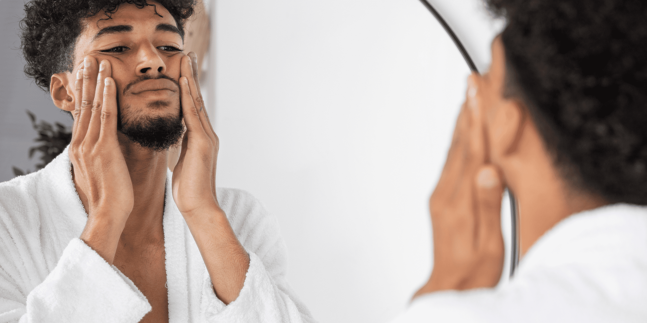 Man in a white robe examining his face in the mirror, focusing on how to get rid of beard dandruff. Showcasing a clean, well-maintained beard and healthy skin.