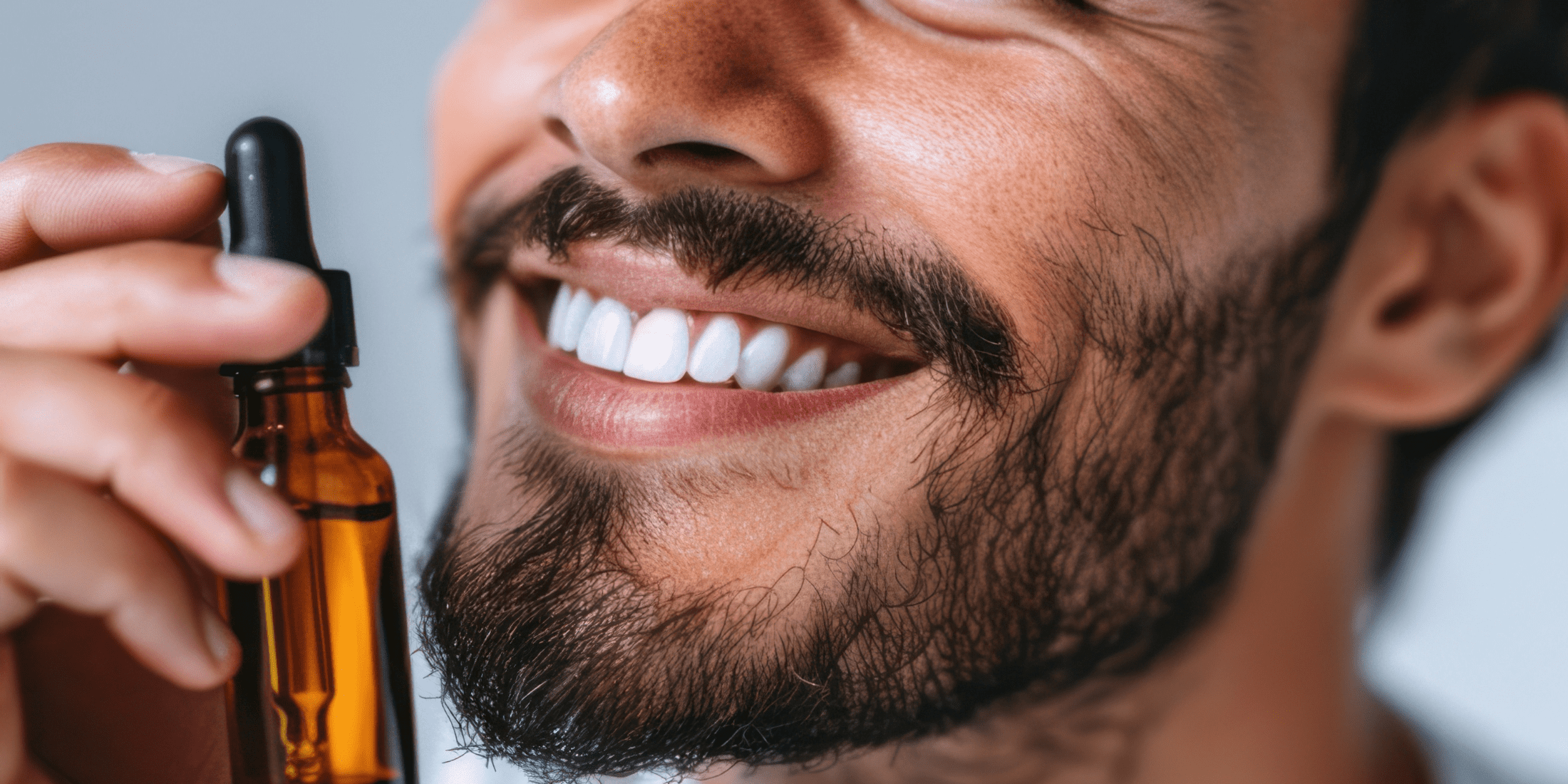 A close-up of a smiling man holding a bottle of beard oil, illustrating how often you should apply beard oil for optimal beard health.