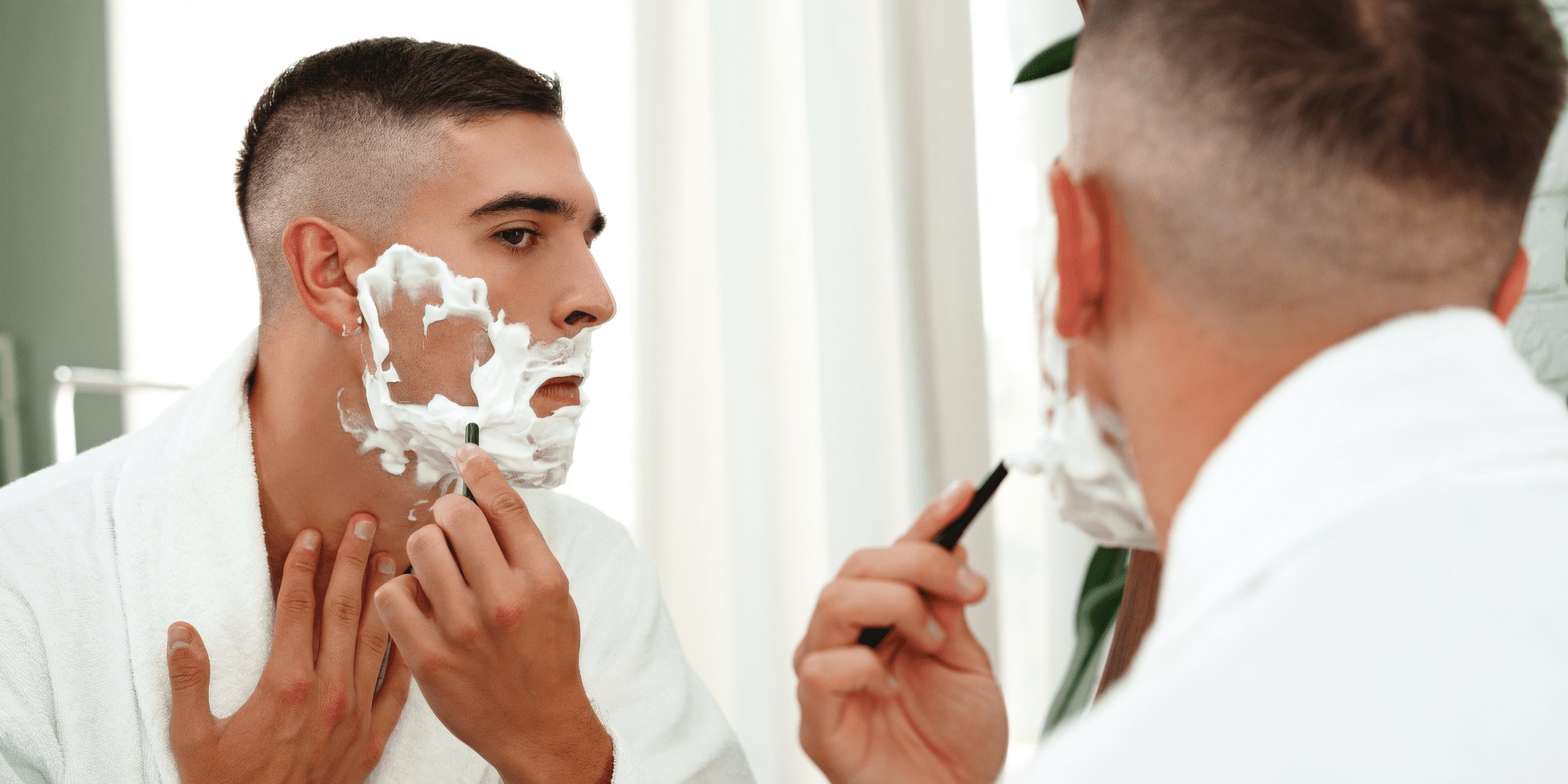 A man looking in the mirror while shaving with shaving cream on his face. This image illustrates what does shaving cream do? by showing its use in providing a smooth and comfortable shaving experience.