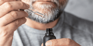 A man is applying beard oil using a dropper, carefully measuring the amount—a step in determining how often should you apply beard oil for effective beard care.