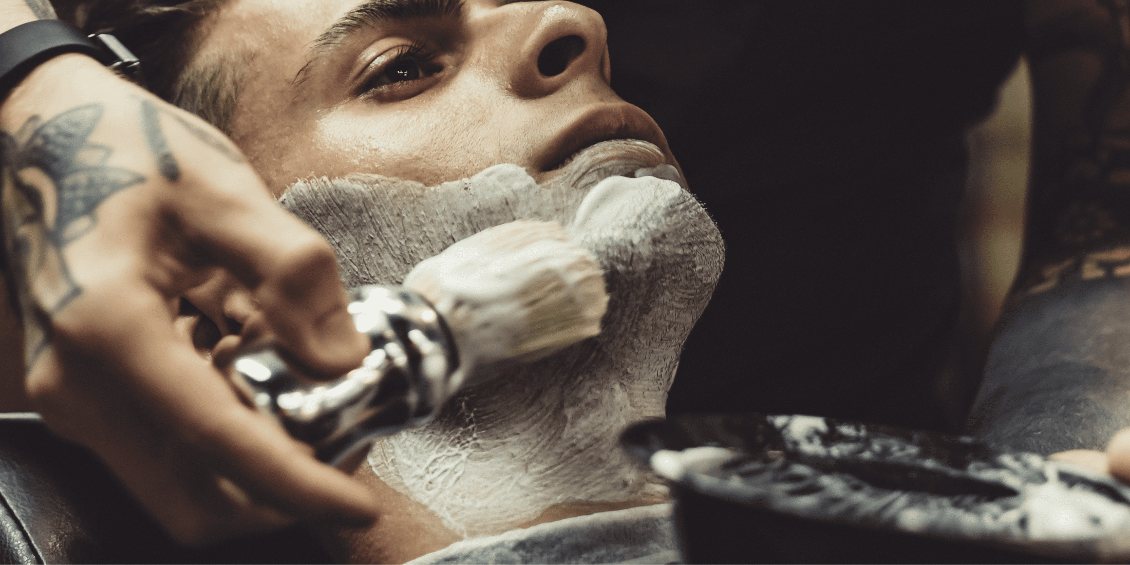 Barber using a shaving brush to apply shaving soap to a client's beard, demonstrating how to use shaving soap and how to lather a shaving soap for a close, comfortable shave