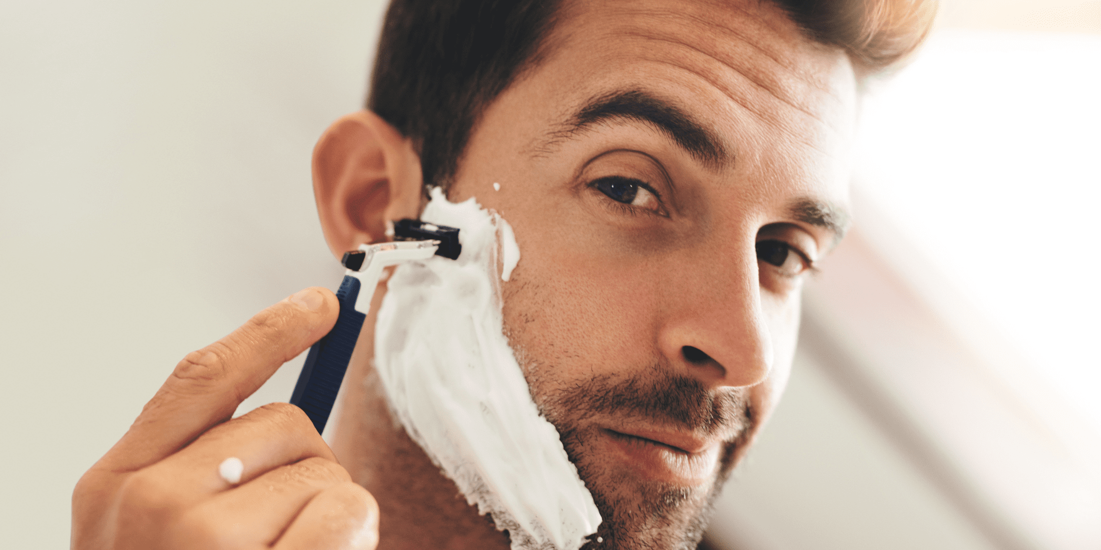 A man shaving his face with a razor, covered in shaving cream. This image demonstrates what does shaving cream do? by showing its application for a smooth and comfortable shave.