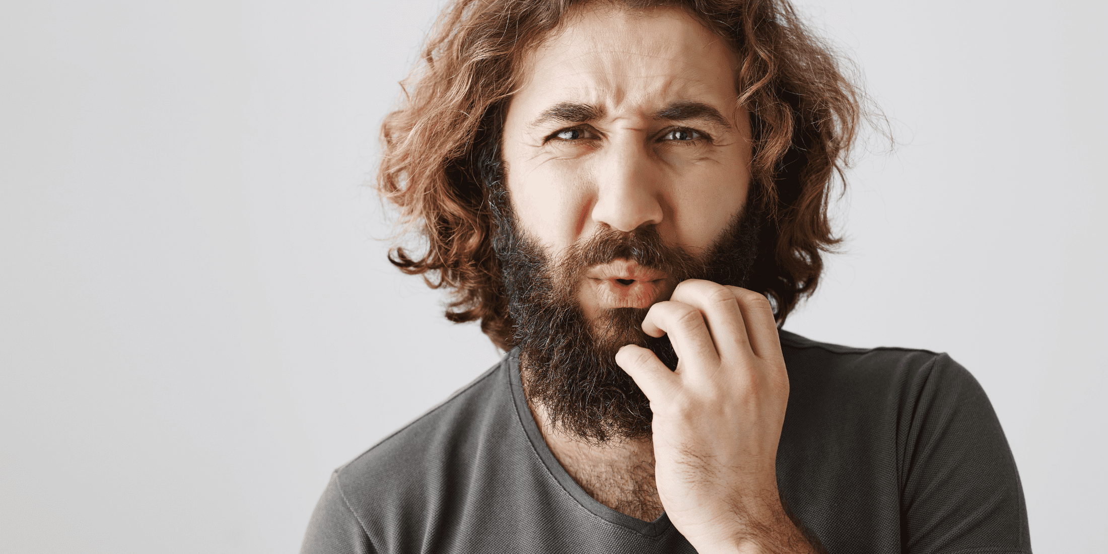 A man with a concerned expression scratches his beard, indicating possible irritation or sores under beard. The image highlights the discomfort and need for effective beard care to address beard sores.