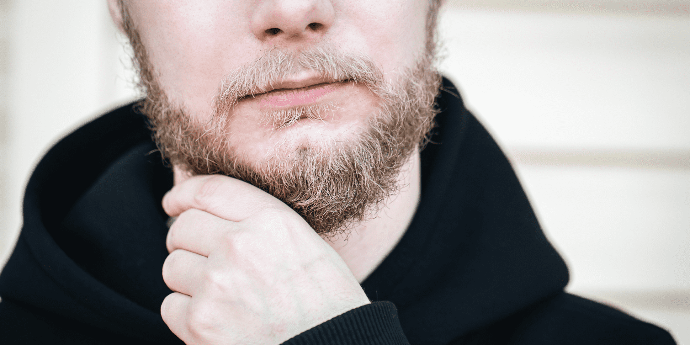 A close-up of a man gently touching his beard, indicating possible irritation or sores under beard. This image emphasizes the importance of proper beard care to prevent and treat beard sores.