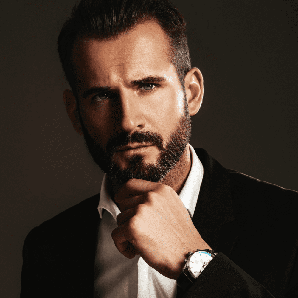 A sophisticated man with a well-groomed medium boxed beard, a popular medium beard style characterized by neat trimming along the jawline and cheekbones. This style offers a clean, structured appearance, perfect for professional and casual settings in 2024. The man's confident pose and elegant attire highlight the refined and polished look provided by the medium boxed beard.