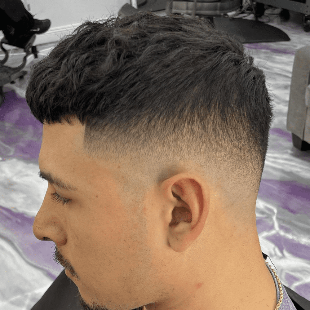 Man with a mid-high drop fade haircut. The hairstyle features a clean, gradual fade starting from the mid to high point of the head, blending seamlessly into the longer, textured hair on top. Ideal for a stylish and modern look, this fade haircut is perfect for men's short fade haircuts in 2024.