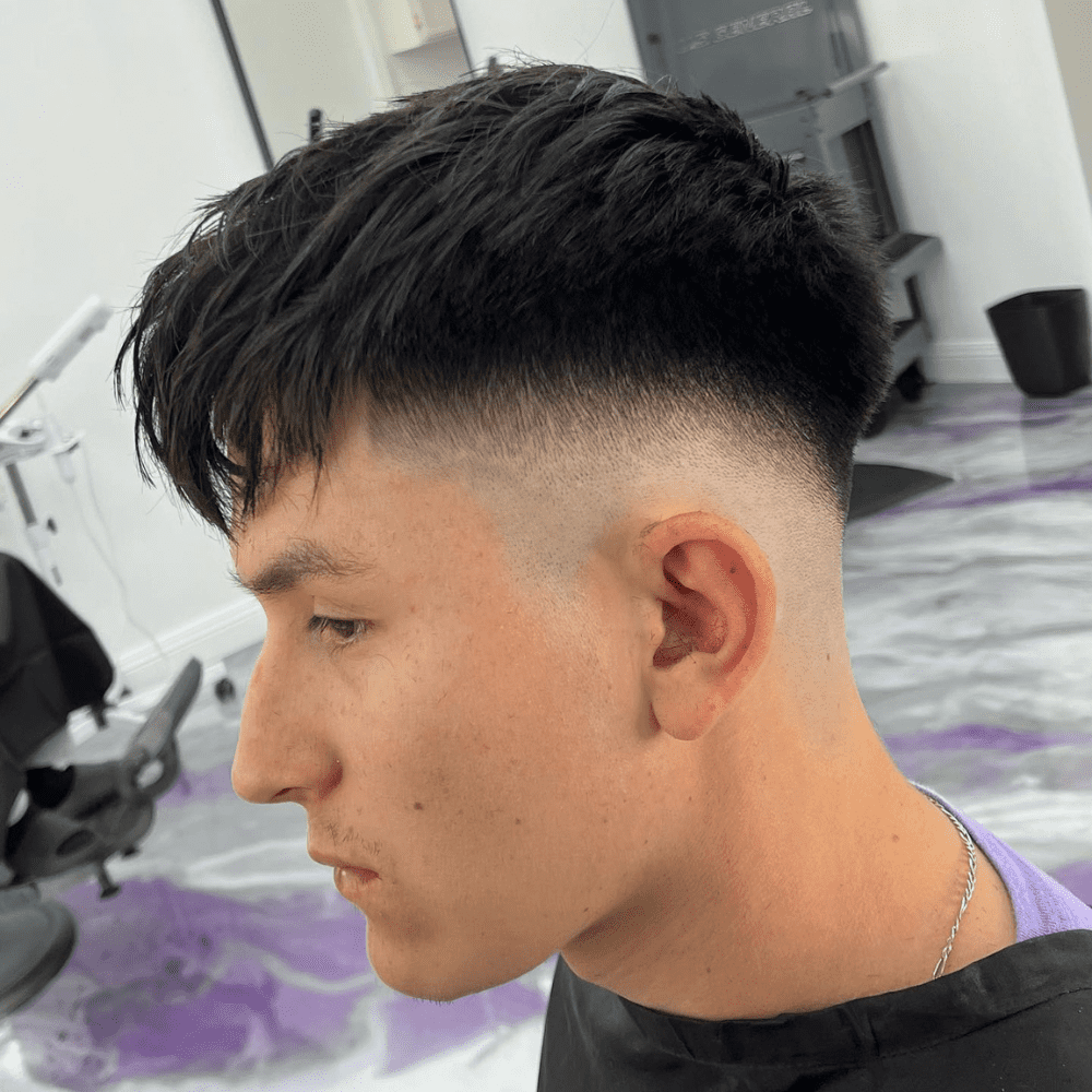 Man with a mid drop fade haircut featuring a textured fringe. The hairstyle includes a clean mid drop fade on the sides and back, blending into the longer, textured fringe on top. Ideal for a modern and stylish look, this mid drop fade with textured fringe is perfect for men's hairstyles in 2024