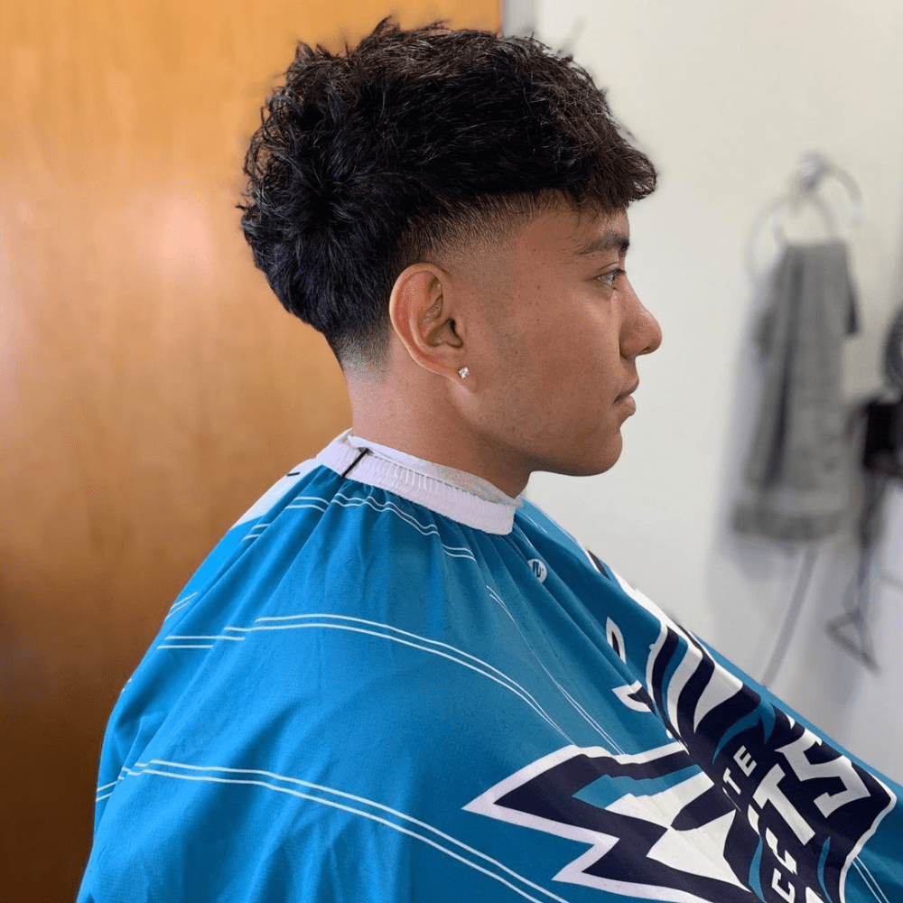 Side profile of a young man with a Mid Taper Fade haircut, featuring thick, textured hair on top with a mid taper fade on the sides and back. The hairstyle provides a balanced and stylish look, making it a popular choice for men seeking trendy fade haircuts