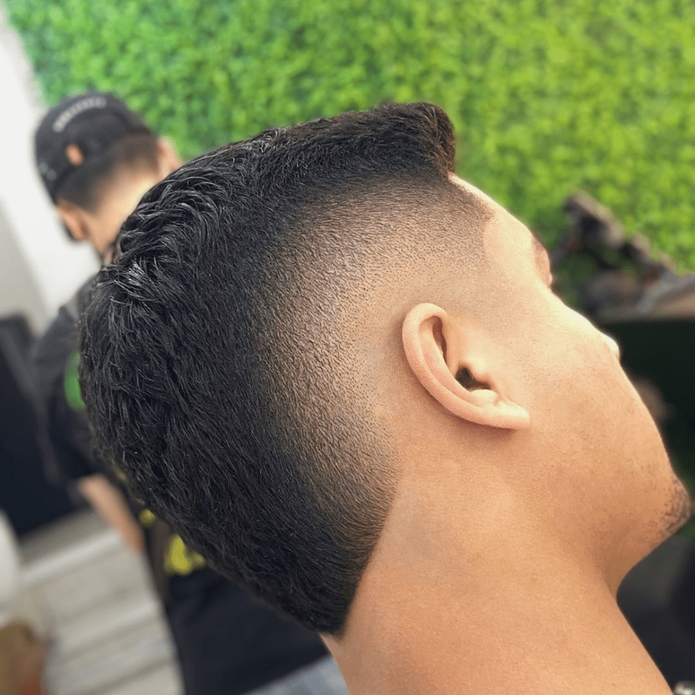 Man with a short fade haircut featuring a mohawk. The hairstyle showcases a clean fade on the sides and back, seamlessly blending into the short, textured mohawk on top. This bold and edgy look is perfect for modern men's hairstyles in 2024, offering a unique and stylish appearance