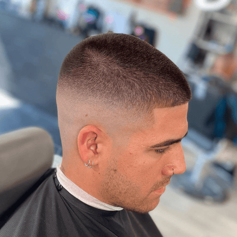 Side profile of a man with a number 3 buzz cut fade, showcasing the clean, uniform length on top transitioning into a smooth fade on the sides and back. The hairstyle highlights his facial features, earrings, and well-groomed appearance, perfect for a modern, stylish look