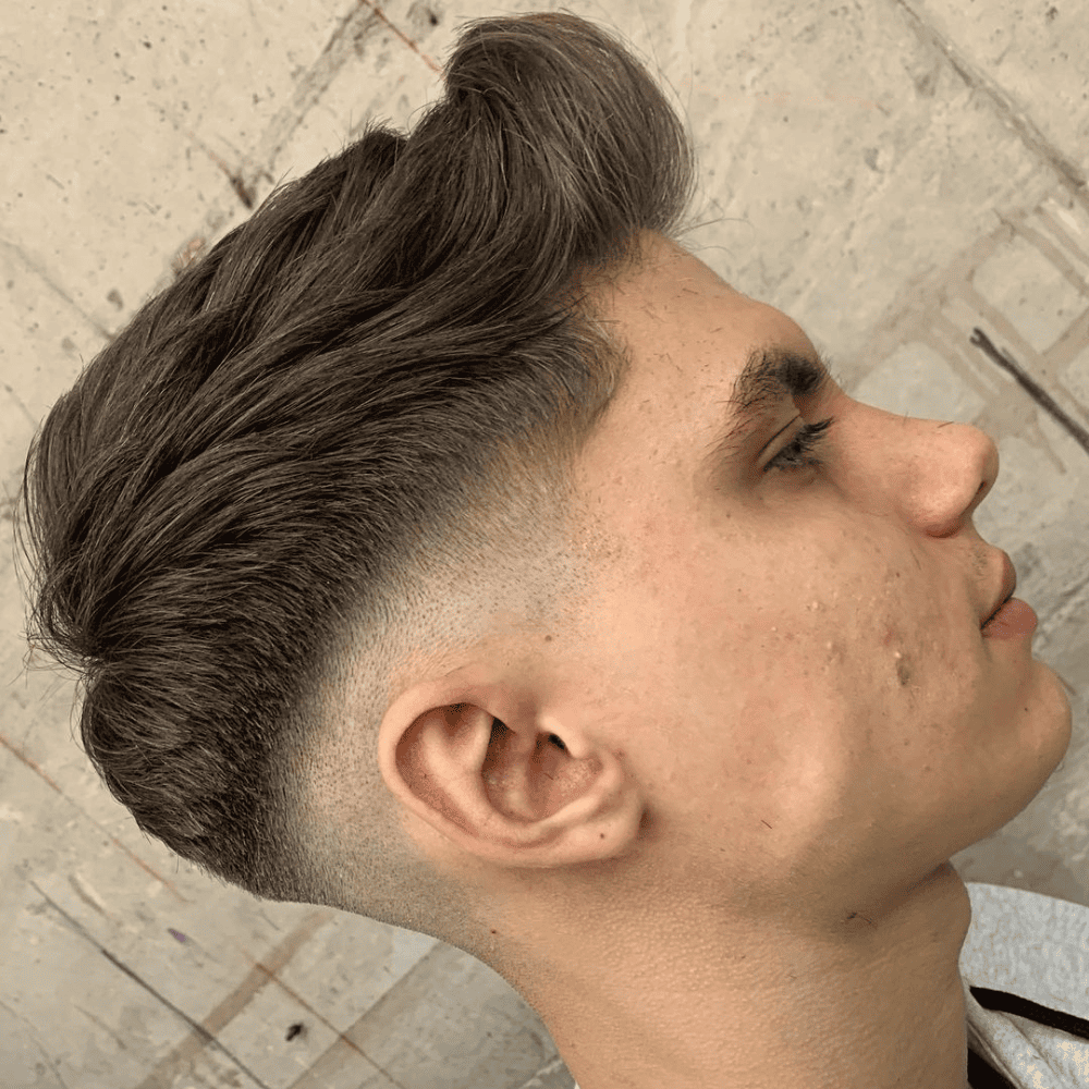 Side profile of a young man with a Mid Fade Quiff haircut, featuring voluminous, textured hair styled up and back on top, combined with a mid fade on the sides and back. The hairstyle offers a stylish and contemporary look, perfect for men seeking trendy fade haircuts