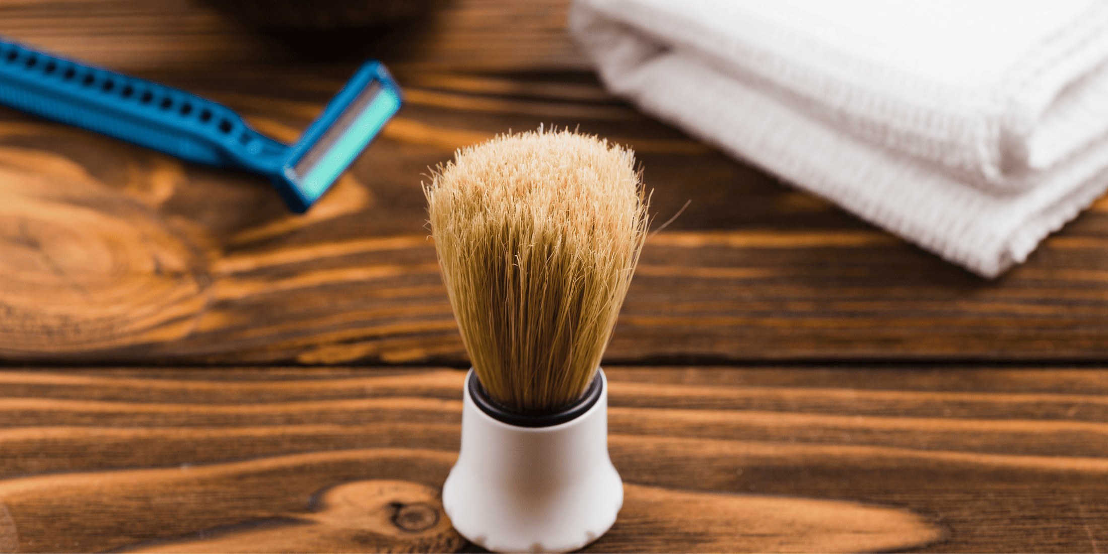 Shaving brush, razor, and hot towel on a wooden surface, showcasing essential tools for learning how to use shaving soap and how to lather a shaving soap for a perfect shave.