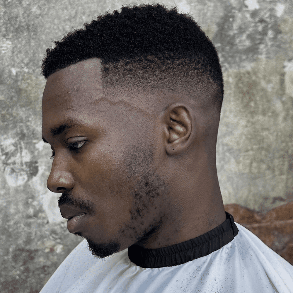 Man with a short fade haircut featuring a short afro. The hairstyle showcases a clean fade on the sides and back, seamlessly blending into the natural, textured afro on top. This modern and stylish look is perfect for men's hairstyles in 2024, highlighting the texture and volume of afro hair.