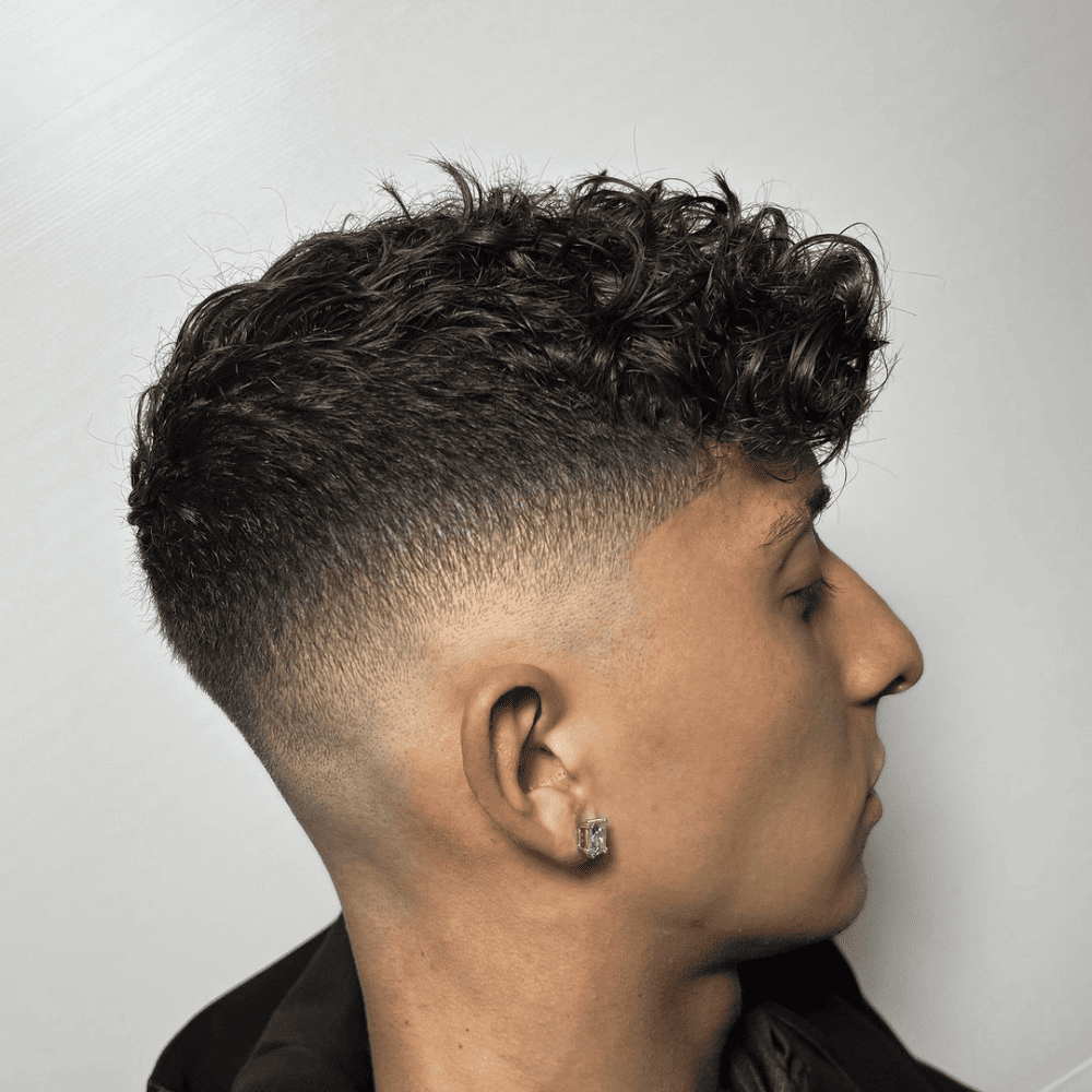 Man with a short fade haircut featuring curly hair on top. The hairstyle showcases a clean, gradual fade on the sides and back, blending into the natural curls on top. This stylish and modern look is ideal for men's hairstyles in 2024, highlighting the texture and volume of curly hair.