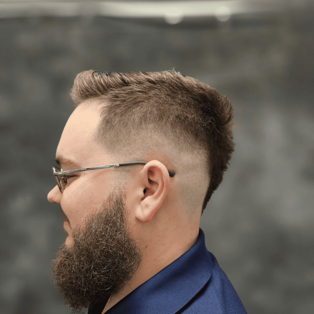 Man with a short fade haircut featuring a faux hawk. The hairstyle includes a clean fade on the sides and back, blending into the textured faux hawk on top. This bold and stylish look is ideal for modern men's hairstyles in 2024, offering a unique and edgy appearance.