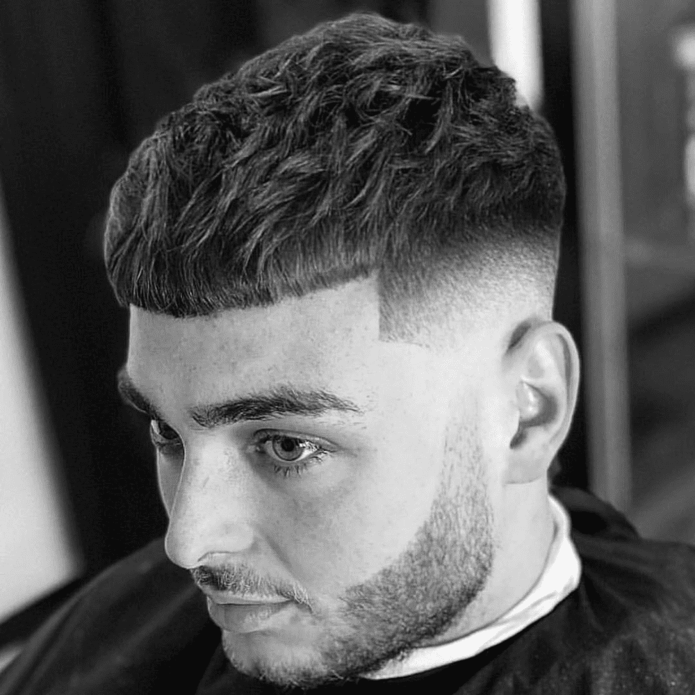 Man with a short fringe haircut featuring a high fade. The hairstyle includes a textured, short fringe on top with a sharp high fade on the sides and back. This modern and stylish look is ideal for men's short fade haircut in 2024, providing a clean and edgy appearance.