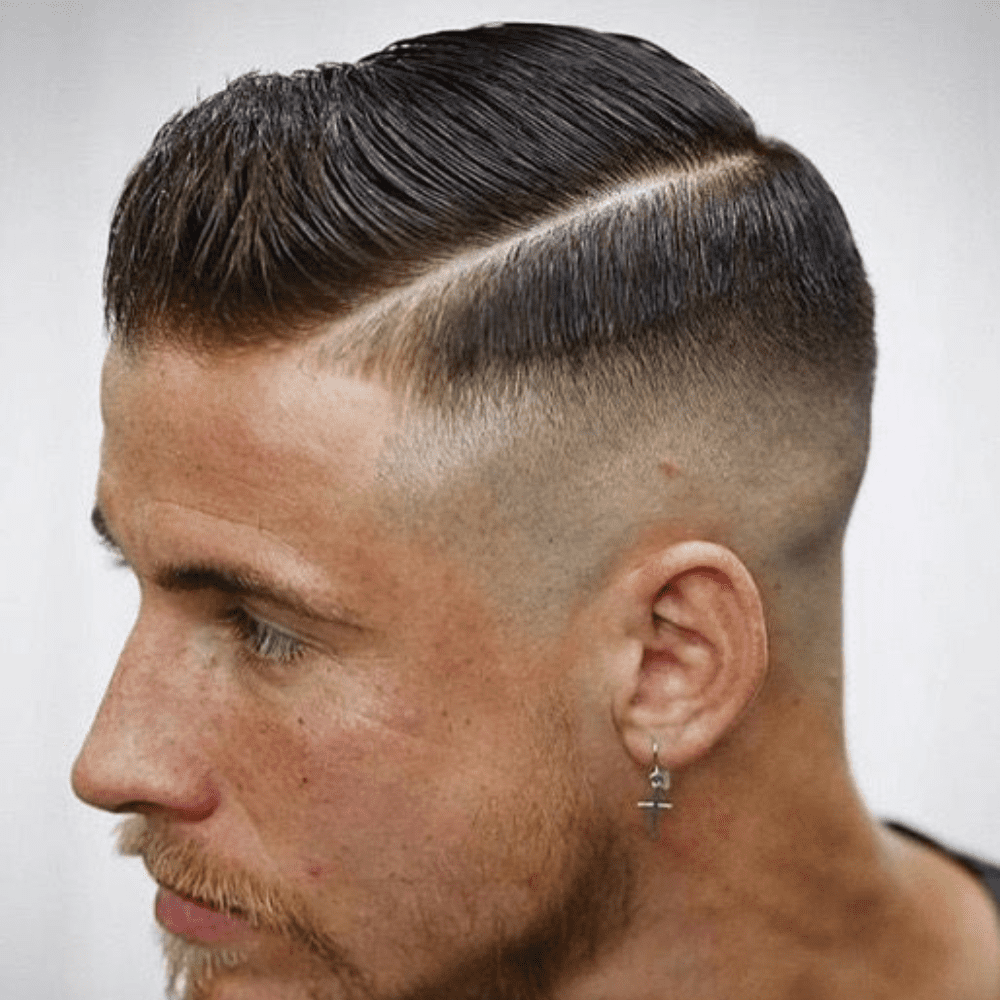 Man with a short side part haircut featuring a sharp parting line and a high fade. The hairstyle highlights a sleek and clean look, complemented by facial hair and an earring, ideal for modern men's hairstyles in 2024