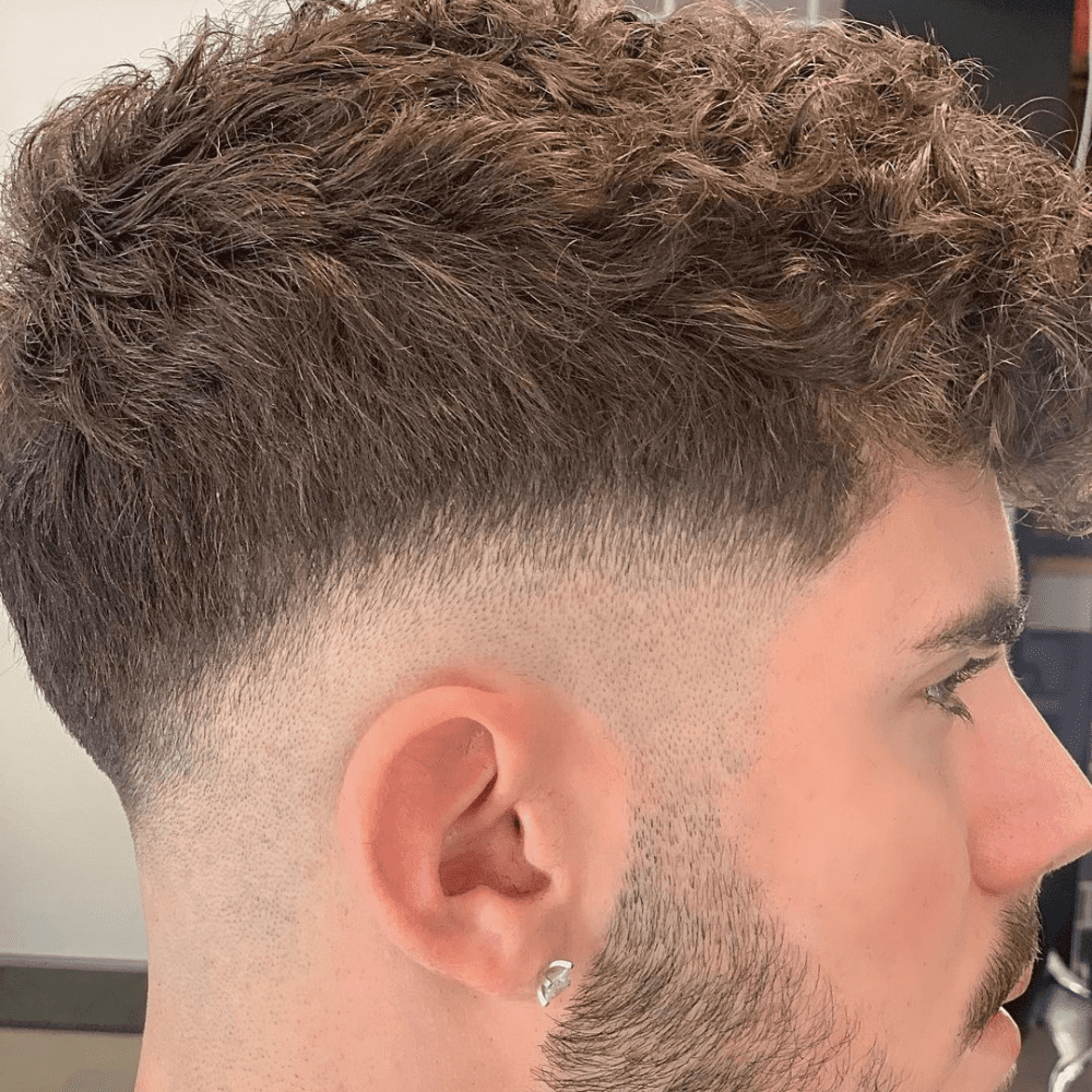 Man with a short thick hair haircut featuring a mid skin fade. The hairstyle showcases voluminous, textured hair on top with a clean, gradual fade on the sides and back. Ideal for highlighting natural curls and achieving a modern, stylish look for men's hairstyles in 2024.