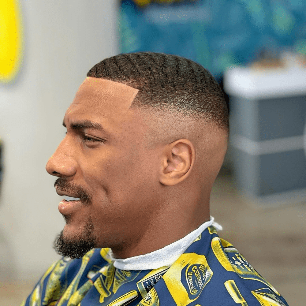 Man with a short fade haircut featuring a clean lineup and waved hair. The hairstyle showcases a smooth fade on the sides and back, blending into the short, waved hair on top. This stylish and modern look is ideal for men's hairstyles in 2024, highlighting the texture and precision of a well-executed fade haircut.