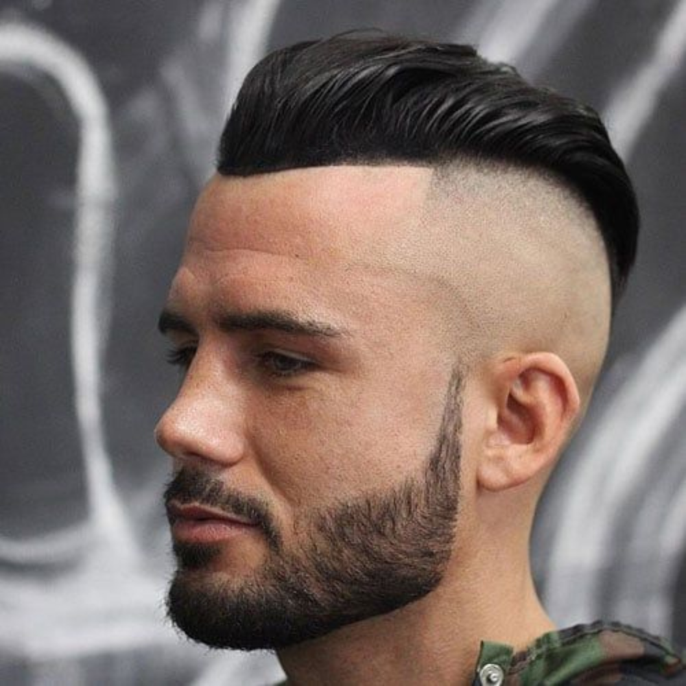 Side profile of a man with a skin undercut slicked back haircut, featuring a dramatic contrast between the shaved sides and the longer, slicked back top. He has a neatly trimmed beard, enhancing the bold and edgy look. This image showcases a striking variation of the slicked back hairstyle, perfect for men in 2024 seeking a modern and daring appearance.