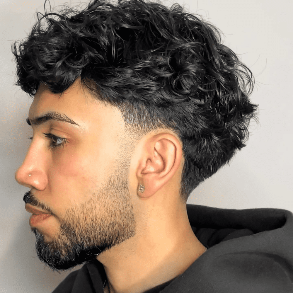 This image highlights a stylish Tapered Curls haircut for men, featuring naturally curly hair that gradually shortens from the top to the sides and back. The tapering effect provides a clean, polished look while enhancing the natural curl pattern. Ideal for men seeking a professional yet trendy style, this haircut works well with various face shapes and is easy to maintain. The tapered curls offer a modern twist on classic curly hairstyles, making it a popular choice for 2024.