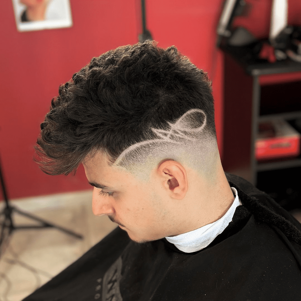 ide profile of a young man with a Tattoo Fade haircut, featuring textured hair on top with intricate shaved designs on the faded sides. The hairstyle combines a modern fade with artistic hair tattoos, making it a bold and unique choice for men seeking trendy fade haircuts.