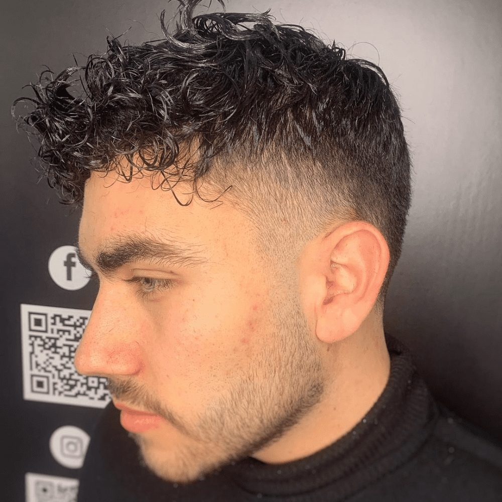 Side profile of a young man with a Temple Fade haircut, featuring short, textured curly hair on top and a clean fade around the temples. The hairstyle offers a modern and fresh look, perfect for men seeking stylish fade haircuts