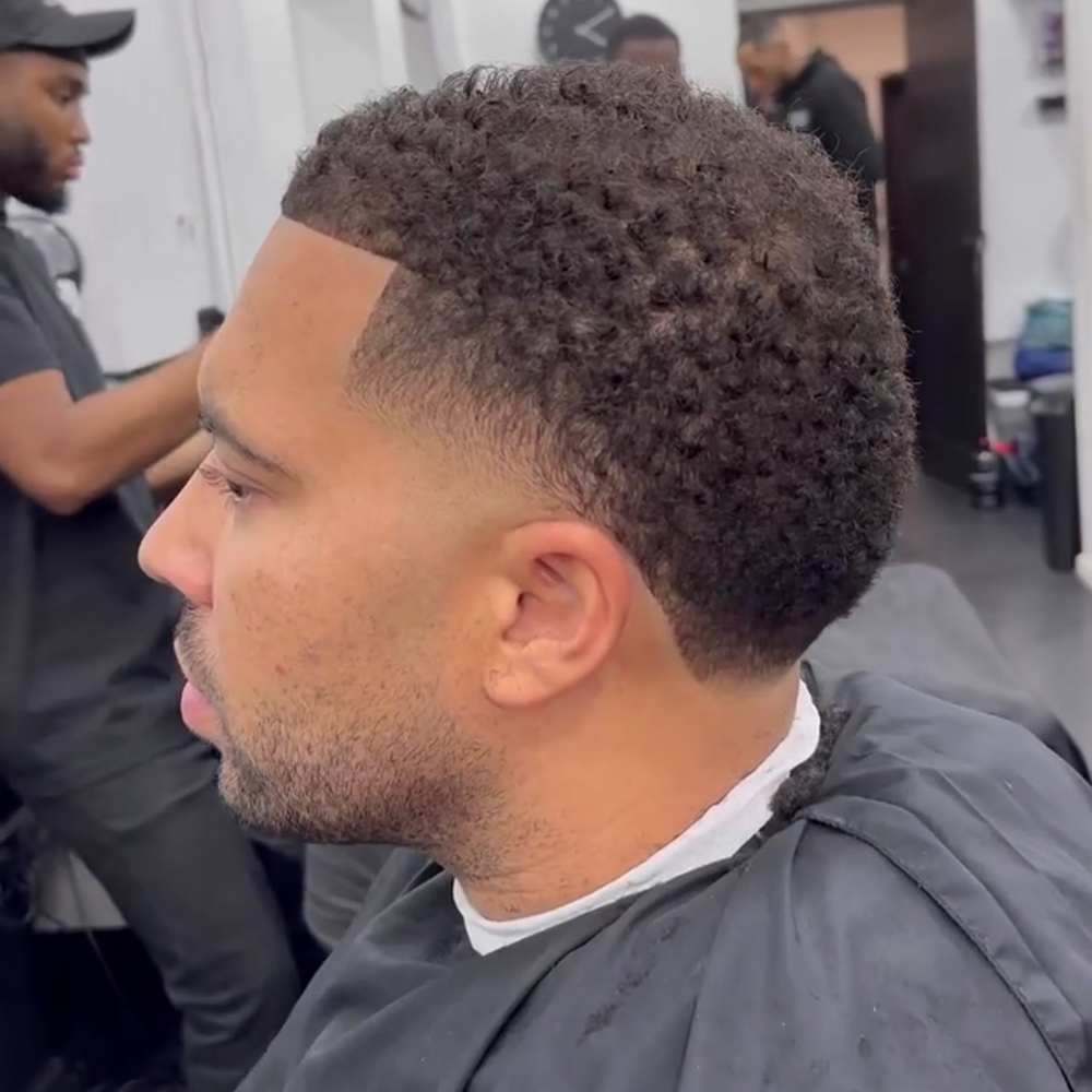 Man with a short fade haircut featuring a high taper (temple fade). The hairstyle includes a clean, gradual fade at the temples, blending into the natural, textured hair on top. This stylish and modern look is perfect for men's hairstyles in 2024, highlighting the precision and detail of a well-executed fade haircut.