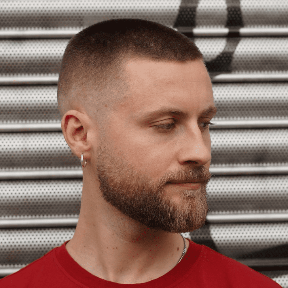 Man with a very short fade haircut featuring a clean, close fade on the sides and back. The hairstyle blends seamlessly into the short length on top, complemented by a well-groomed beard. This low-maintenance and stylish look is perfect for modern men's hairstyles in 2024, offering a sharp and polished appearance.